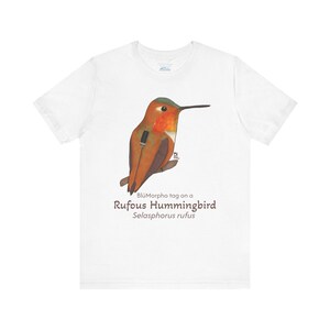 May include: White t-shirt with a colorful illustration of a Rufous Hummingbird, with the text "BluMorpho tag on a Rufous Hummingbird Selasphorus rufus".