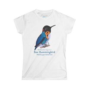 May include: White t-shirt featuring a detailed illustration of a Bee Hummingbird, with blue, black, and orange plumage, perched on a branch. The text "BlüMorpho tag on a Bee Hummingbird Mellisuga helenae" is printed below the bird.