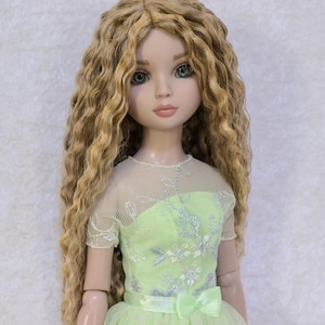 May include: A doll with long, wavy blonde hair wearing a light green dress with a tulle overlay. The dress features silver embroidery and a matching bow. The doll is wearing white shoes. The text "JodieCreations" is at the bottom.