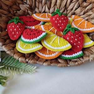 Puede incluir: Una cesta de mimbre llena de fruta de ganchillo, incluyendo fresas y rodajas de naranja. La fruta está hecha con hilo rojo, amarillo y verde.