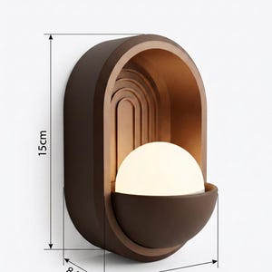 May include: A dark brown wall sconce featuring an arched frame with a nested rainbow design and a central white spherical light bulb. The fixture measures 15 cm in height, 10 cm in width, and 8.5 cm in depth as indicated by the technical lines.