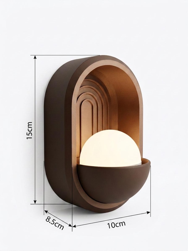 May include: A dark brown wall sconce featuring an arched frame with a nested rainbow design and a central white spherical light bulb. The fixture measures 15 cm in height, 10 cm in width, and 8.5 cm in depth as indicated by the technical lines.