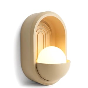 May include: A wall-mounted light fixture featuring a matte beige, arched frame with concentric semi-circular grooves. A glowing, spherical white glass bulb sits within a semi-circular base, casting a warm, soft light against the arched interior.