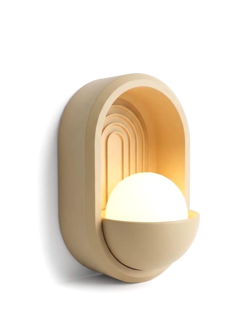 May include: A wall-mounted light fixture featuring a matte beige, arched frame with concentric semi-circular grooves. A glowing, spherical white glass bulb sits within a semi-circular base, casting a warm, soft light against the arched interior.