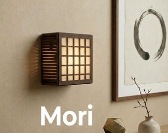 May include: A square wall-mounted lamp with a dark brown wooden frame and a grid-patterned translucent shade that emits a warm glow. The word Mori is printed in white text below the lamp. The lamp features horizontal slats on the side.