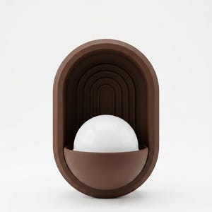 May include: A wall-mounted lamp featuring a matte brown oval frame with a recessed arched interior design. A white hemispherical glass globe sits within a matching brown semi-circular base at the bottom of the fixture, creating a layered look.