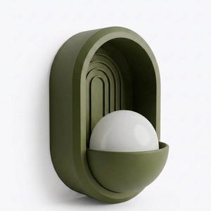 May include: An olive green wall sconce featuring an arched, recessed back panel with concentric semi-circular grooves. A semi-spherical, matte olive green base holds a smooth, opaque white spherical light bulb in the center of the fixture.