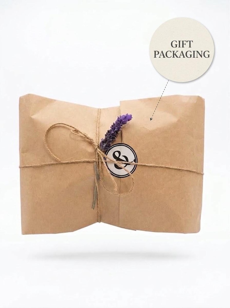 May include: A rectangular package wrapped in brown kraft paper, tied with thin twine. A sprig of purple lavender is tucked under the twine next to a circular white sticker featuring a black ampersand symbol. A circular label above reads GIFT PACKAGING.