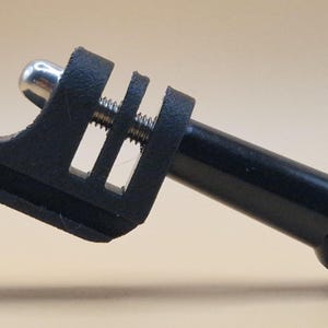 May include: A black camera mount with a silver screw and a cylindrical extension. The mount has a clamp-like design with a slotted section and a rounded end. The product is designed to attach to a camera.