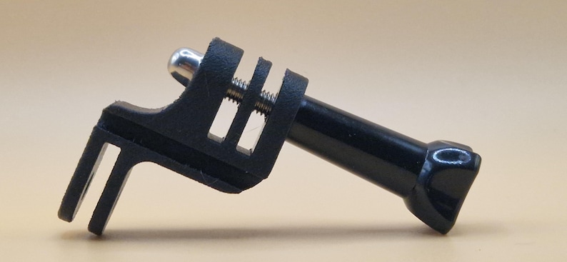 May include: A black camera mount with a silver screw and a cylindrical extension. The mount has a clamp-like design with a slotted section and a rounded end. The product is designed to attach to a camera.