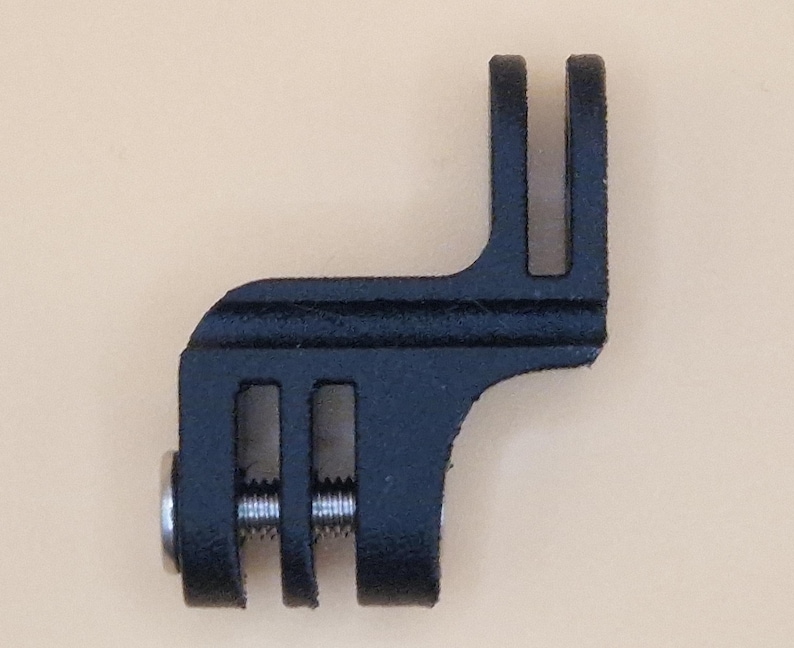 May include: A black metal bracket with a slotted design and a silver screw. The bracket has a right-angle shape with two parallel slots on one end and a single slot on the other. The item is likely a mounting component.