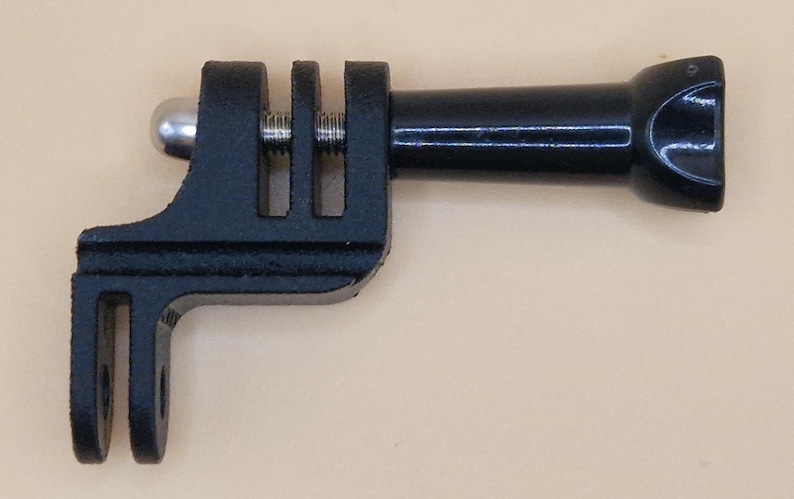 May include: A black camera mount adapter with a ball joint, screw, and a rectangular base with two slots. The adapter has a cylindrical extension with a curved end. The item is designed to attach to a camera.