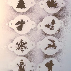 May include: A collection of Christmas-themed stencils. Designs include a Christmas tree, Santa in a sleigh, an angel, holly, a snowflake, a reindeer, a snowman, and Santa carrying a sack. The stencils are white with brown designs, perfect for holiday crafts.