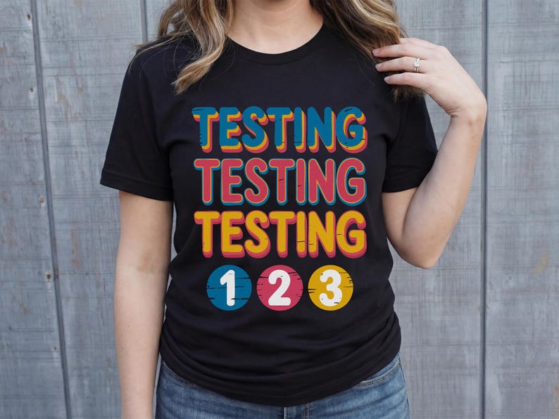Puede incluir: Camiseta negra con la palabra "TESTING" repetida tres veces en una tipograf&iacute;a retro colorida. Debajo, los n&uacute;meros "1 2 3" en c&iacute;rculos. Una prenda casual para el d&iacute;a a d&iacute;a.