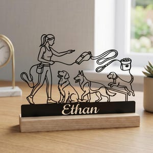 May include: A black laser-cut dog-themed desk ornament featuring a person walking three dogs, with a leash and food bowl. The name "Ethan" is displayed on the base. The ornament is set on a wooden base.