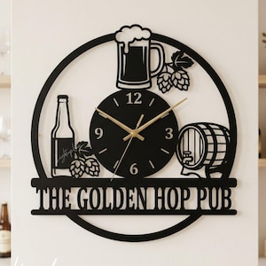 Może przedstawiać: Czarny metalowy zegar ścienny z motywem piwa. Zegar przedstawia kufel piwa, butelkę, chmiel i beczkę. Tekst "THE GOLDEN HOP PUB" jest wyświetlany poniżej tarczy zegara. Wskazówki są złote.