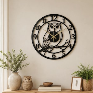Peut inclure: Une horloge murale noire et circulaire avec un motif de hibou découpé. L'horloge a des aiguilles et des chiffres dorés. L'horloge est fixée sur un mur de couleur claire au-dessus d'une étagère en bois avec des objets décoratifs.