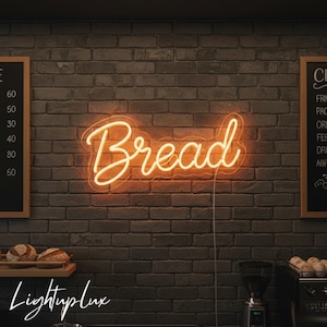 May include: A neon sign in warm orange light spells out the word "Bread" in a cursive font. The sign is mounted on a dark brick wall. The image also shows a wooden shelf with bread loaves and a sign that says "Lightuplux".