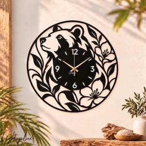 May include: A circular black wall clock featuring a laser-cut silhouette of a bear head surrounded by floral and leaf patterns. The clock face is black with white numerals at 12, 3, 6, and 9, gold-colored hands, and the text Lightuplux.