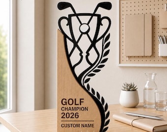 Könnte beinhalten: Eine dekorative Trophäe mit einem hellen Holzsockel, auf dem der Text GOLF CHAMPION 2026 und CUSTOM NAME eingraviert ist. Eine schwarze Silhouette eines Pokals mit gekreuzten Golfschlägern und Lorbeerblatt-Design ragt aus dem Holzsockel hervor.