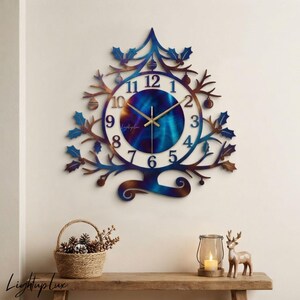 May include: A wall clock shaped like a stylized tree with holly leaves and ornaments. The clock face features a blue and bronze gradient center with white numbers from 1 to 12 and gold hands. The metal frame has a blue and bronze finish.