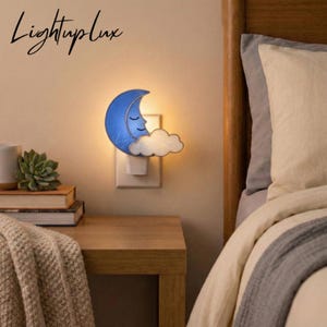 May include: A blue crescent moon night light with a smiling face and a white cloud, plugged into a wall outlet. The text "LightupLux" is in the upper left corner. The night light is on a wooden nightstand next to a bed.