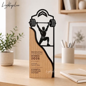 May include: A trophy featuring a light wood base with black text reading WEIGHTLIFTING CHAMPIONSHIP WINNER 2026, CATEGORY: MEN'S 73KG, STRENGTH DISCIPLINE VICTORY. A black metal silhouette of a person lifting a barbell is attached to the wood.