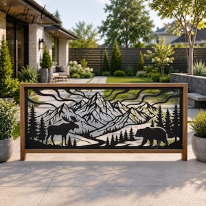 May include: A rectangular metal privacy screen featuring a laser-cut design of a mountain range, a moose, a bear, and pine trees, framed in a light-colored wooden border. The black metal panel displays a detailed wilderness landscape scene.