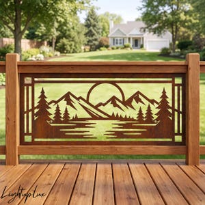 May include: A rectangular metal railing insert featuring a laser-cut design of a mountain range, a circular sun, and pine trees reflected in a body of water. The metal has a rusted brown finish and is framed by a wooden deck railing structure.