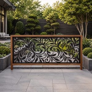May include: A rectangular outdoor privacy screen featuring a black metal panel with an intricate laser-cut floral and vine pattern, framed by a natural wood border. The screen stands on a light-colored stone patio with a garden view.