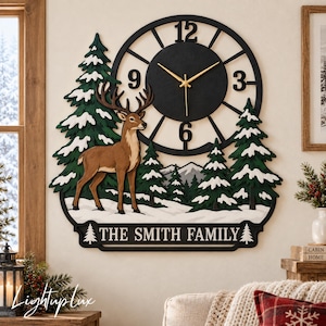 May include: A wall clock featuring a black circular frame with gold hands, a brown deer standing in a snowy forest with green pine trees, and a bottom plaque with the text THE SMITH FAMILY flanked by two small pine tree icons.
