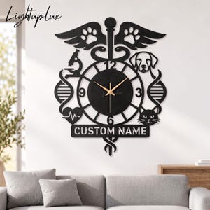 Könnte beinhalten: Eine schwarze Wanduhr mit einem zentralen runden Zifferblatt und goldenen Zeigern, umgeben von einem ausgeschnittenen Design mit einem Caduceus, einem Mikroskop, einem DNA-Strang, einer Herzlinie, einem Hund, einer Katze und dem Text CUSTOM NAME.