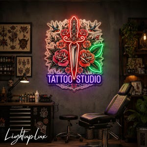 May include: A rectangular neon sign featuring a central dagger surrounded by red roses and two swallows, with the text TATTOO STUDIO in purple neon at the bottom. The design is illuminated with vibrant red, green, and purple light against a dark wall.