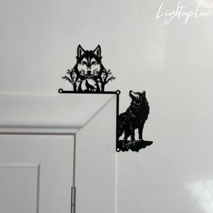 Könnte beinhalten: Zwei schwarze Wanddekorationen aus Metall in Form von Wolfssilhouetten. Ein Wolf heult und der andere schaut zur Seite. Beide sind an einer weißen Wand montiert.