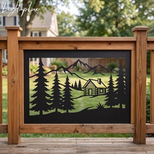 May include: A rectangular black metal panel featuring a laser-cut design of a mountain range, a small log cabin, and several pine trees. The panel is framed by a natural brown wooden railing with vertical posts and horizontal beams.