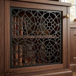Puede incluir: Una puerta de armario de madera oscura con una rejilla metálica negra de patrón circular geométrico. La rejilla cubre un espacio de almacenamiento con varios libros de lomo marrón y decantadores de cristal. Tiene un pequeño pomo de latón.