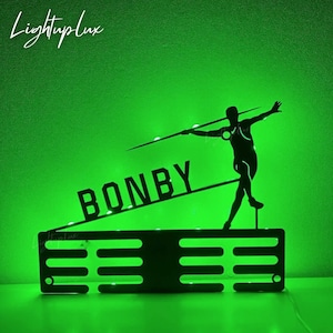 May include: A black silhouette of a person throwing a javelin, with the name "BONBY" in bold letters. The design is illuminated with green lights, set against a vibrant green background. The text "Lightuplux" is in the upper left corner.