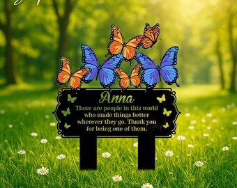 Può includere: Un cartello da giardino rettangolare nero con bordi decorativi, che riporta il nome Anna e il testo: There are people in this world who made things better wherever they go. Thank you for being one of them. Decorato con farfalle arancioni e blu.