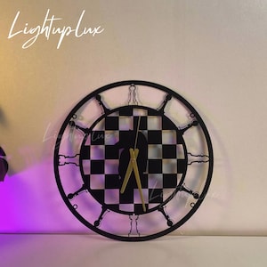 May include: Black and white chessboard clock with gold hands. The clock is shaped like a circle and has a black frame. The chessboard is in the center of the clock and the hands are pointing to the time.