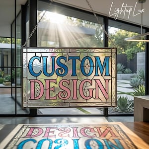 May include: A rectangular stained glass panel with the words "CUSTOM DESIGN" in blue and pink. The panel is suspended by a chain in front of a window, with sunlight streaming through. The style is reminiscent of Art Nouveau.