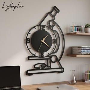 Könnte beinhalten: Eine schwarze Wanduhr in Form eines Mikroskops mit rundem Zifferblatt, goldfarbenen Zeigern und den Ziffern 3, 6, 9 und 12. Die Uhr hat ein lineares Rahmendesign und der Text Lightuplux ist in der oberen linken Ecke zu sehen.