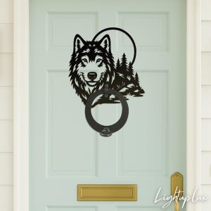 Könnte beinhalten: Schwarzer Metall-Türklopfer mit einem Wolfskopf, Bäumen und einem kreisförmigen Design. Der Türklopfer ist an einer hellblauen Tür mit einem goldfarbenen Briefschlitz und Türgriff angebracht. Der Text "Lightuplux" ist unten rechts sichtbar.