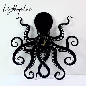 Op de afbeelding: Zwarte octopus wandklok met gouden wijzers en een witte achtergrond. De klok heeft een uitgesneden ontwerp van een octopus met zijn tentakels die de lijst van de klok vormen. De wijzerplaat toont de cijfers 1 tot en met 12.