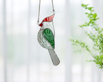 May include: A stained glass bird suncatcher hanging from a metal chain. The bird features a red crest, a white body with textured glass, and a green wing. The text Lightuplux is visible in the upper right corner of the image.