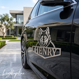 Puede incluir: Un emblema de metal plateado que presenta un gráfico de cabeza de lobo estilizado sobre el texto HENRY en letras mayúsculas negritas, montado en la puerta lateral de un vehículo negro brillante con acabado reflectante y detalles plateados.