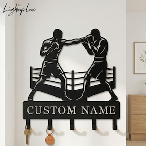 May include: Black metal wall art depicting two boxers in a ring, with the text "CUSTOM NAME" below. Includes hooks for keys and a key ring with the word "HOME". The logo "Lightuplux" is in the upper left corner.