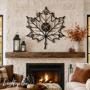 May include: A black metal wall clock shaped like a large maple leaf with thin, dark branches forming the veins. The clock features gold-colored hands and black numerals from one to twelve integrated into the leaf's perimeter, centered on a circular black dial.