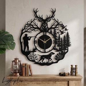 Peut inclure: Horloge murale en métal noir avec un thème de chasse. Elle représente un cerf, un chasseur, un chien et une forêt. Le cadran circulaire a des aiguilles dorées. Le design comprend des arbres, des oiseaux et un chasseur visant avec un fusil.