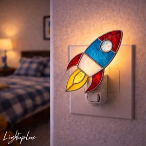 May include: A stained glass rocket night light with red, white, blue, and yellow sections. The rocket is plugged into a white wall outlet. The text "LightupLux" is in the bottom left corner.