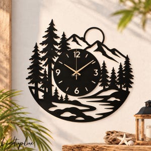 May include: A circular black metal wall clock featuring a silhouette of a mountain range, a sun, and pine trees. The clock face is black with gold-colored hands and numerals at 3, 6, 9, and 12. The text Lightup Lux is printed in small white letters.
